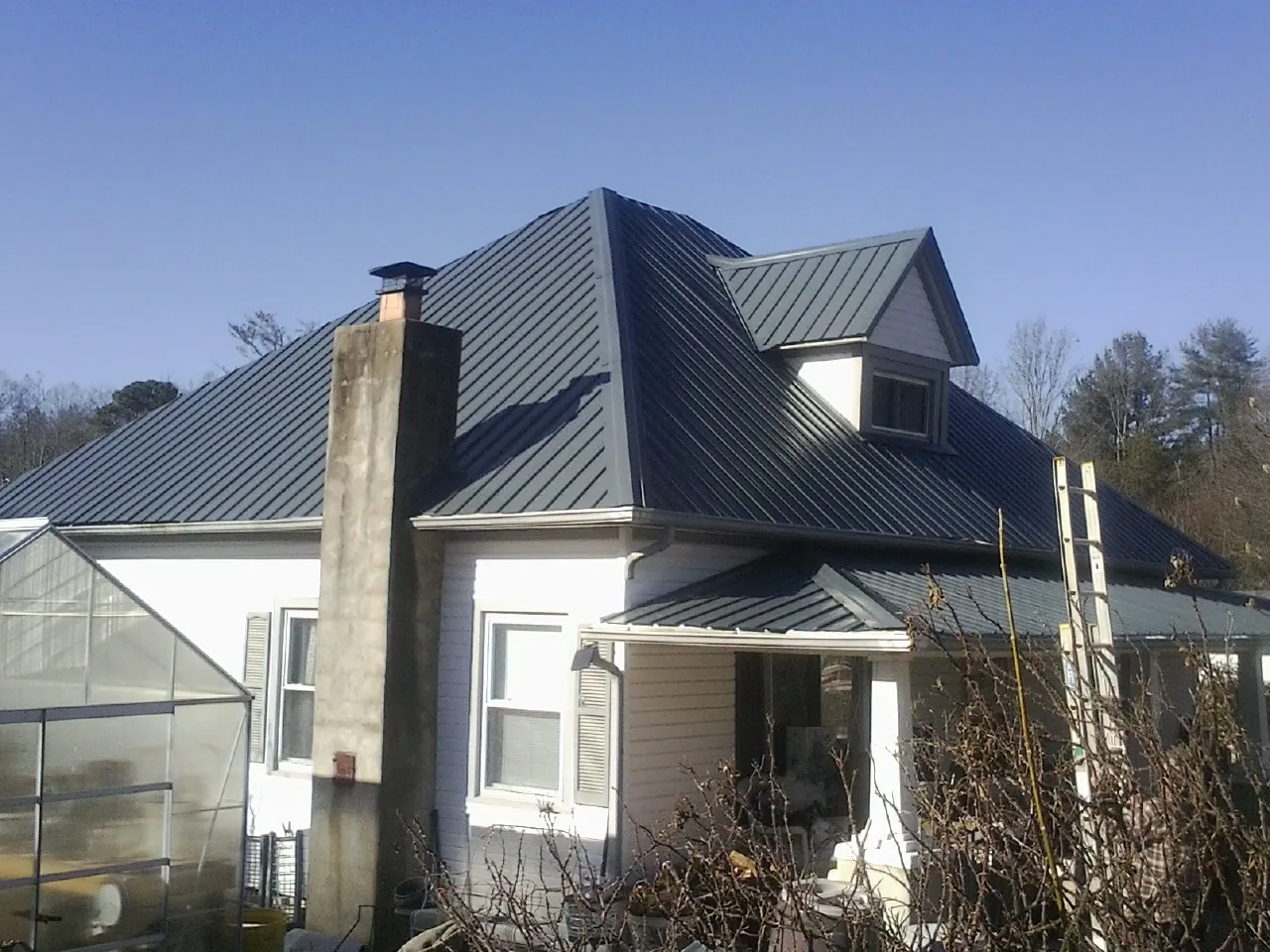 Dark blue standing seam metal roof on a white farmhouse with dormer in Cotopaxi