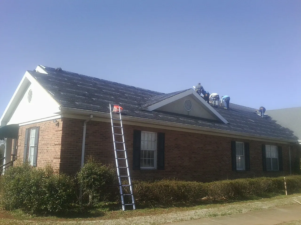 Crew tearing shingles off a brick ranch roof with a ladder set — Metal Roof Repair work by our crew in Cotopaxi