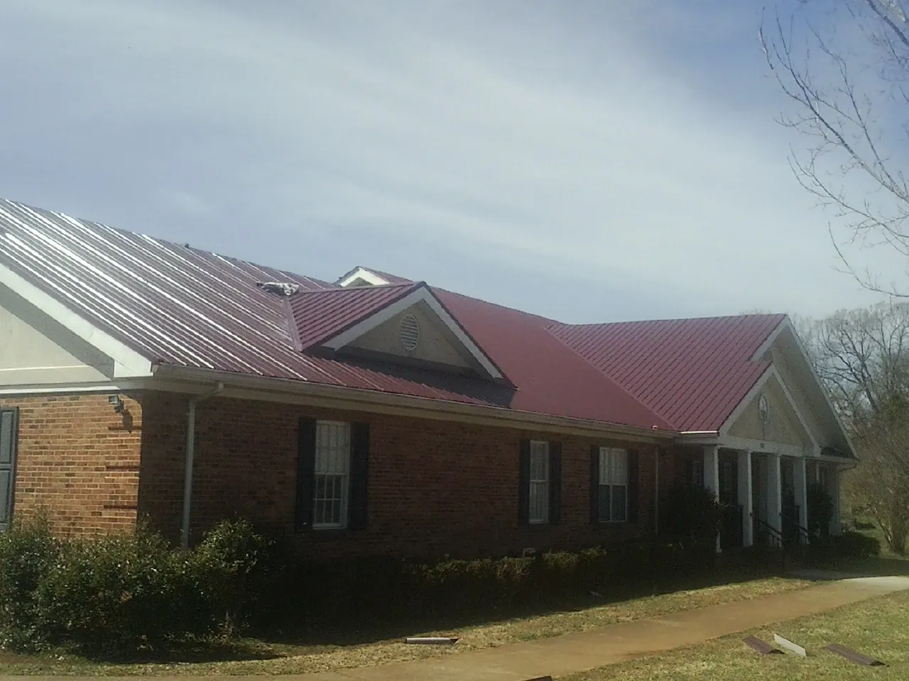 Red metal roof with gabled entries on a long brick building, from a Hail Damage Roof Repair job in Cotopaxi