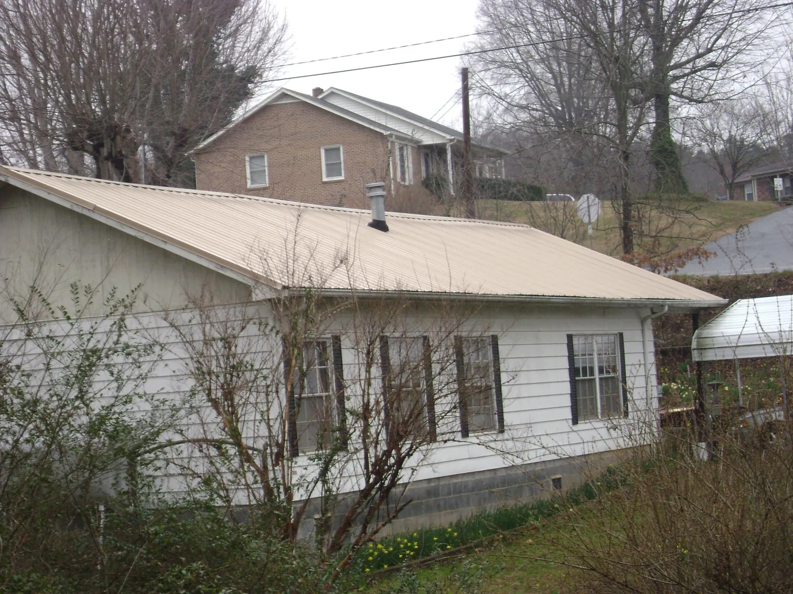 Tan metal roof on a white sided house set into a hillside — Commercial Roofing by Roofing Brothers in Cotopaxi